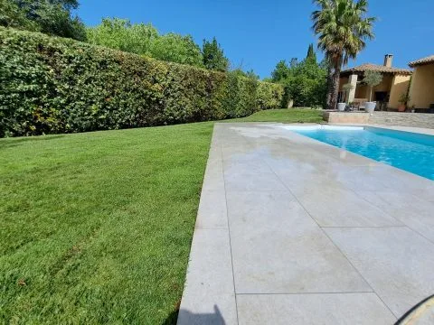 Pose de plaques de pelouse : gazon en plaques posé autour d'une piscine, dalles claires en bordure